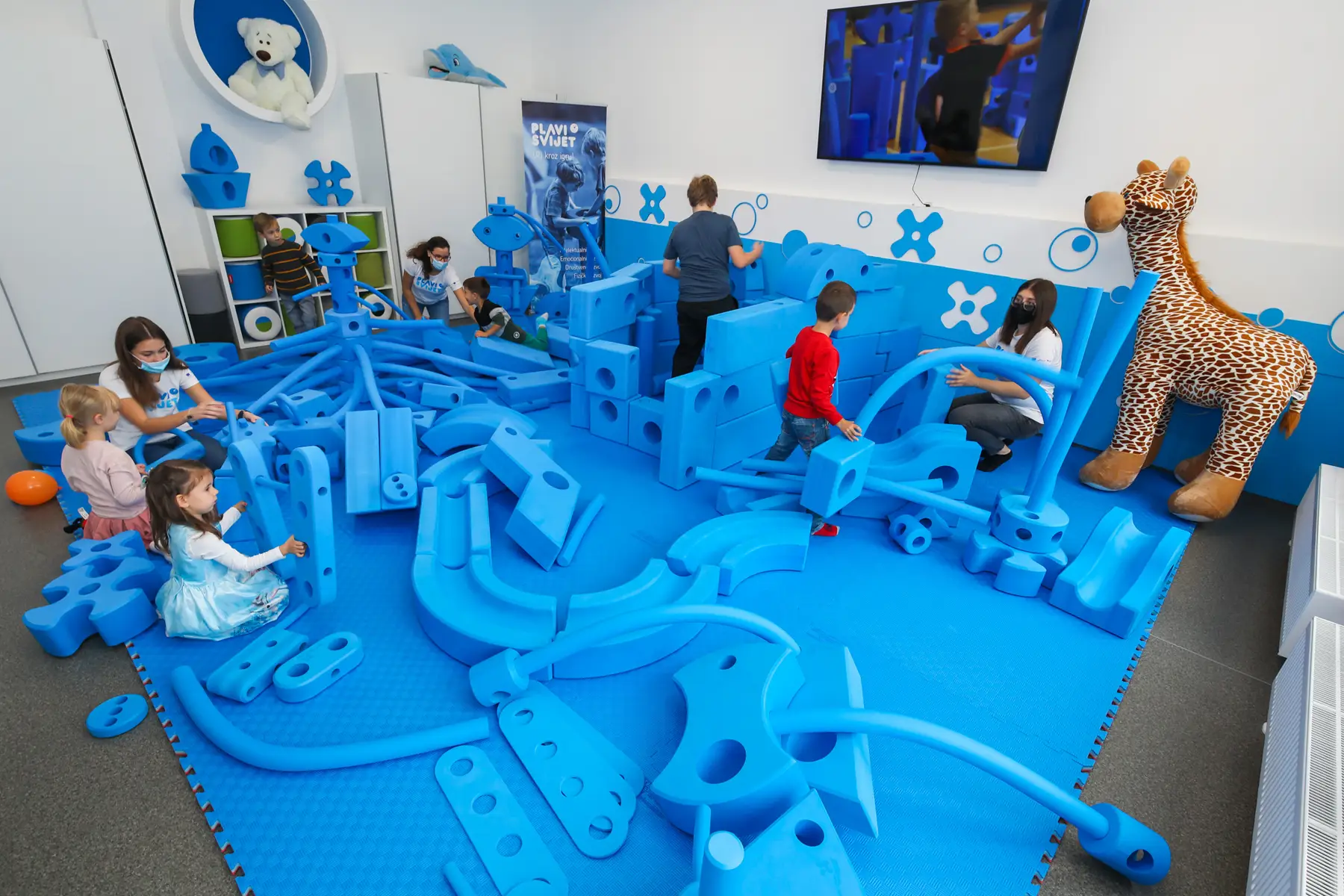 Children exploring geometric concepts through unstructured play with the Big Blue Blocks Angles & Curves set. This modular foam play system is shown in an indoor setting, highlighting how these loose parts allow for more advanced, mechanical-style connections and creative construction.