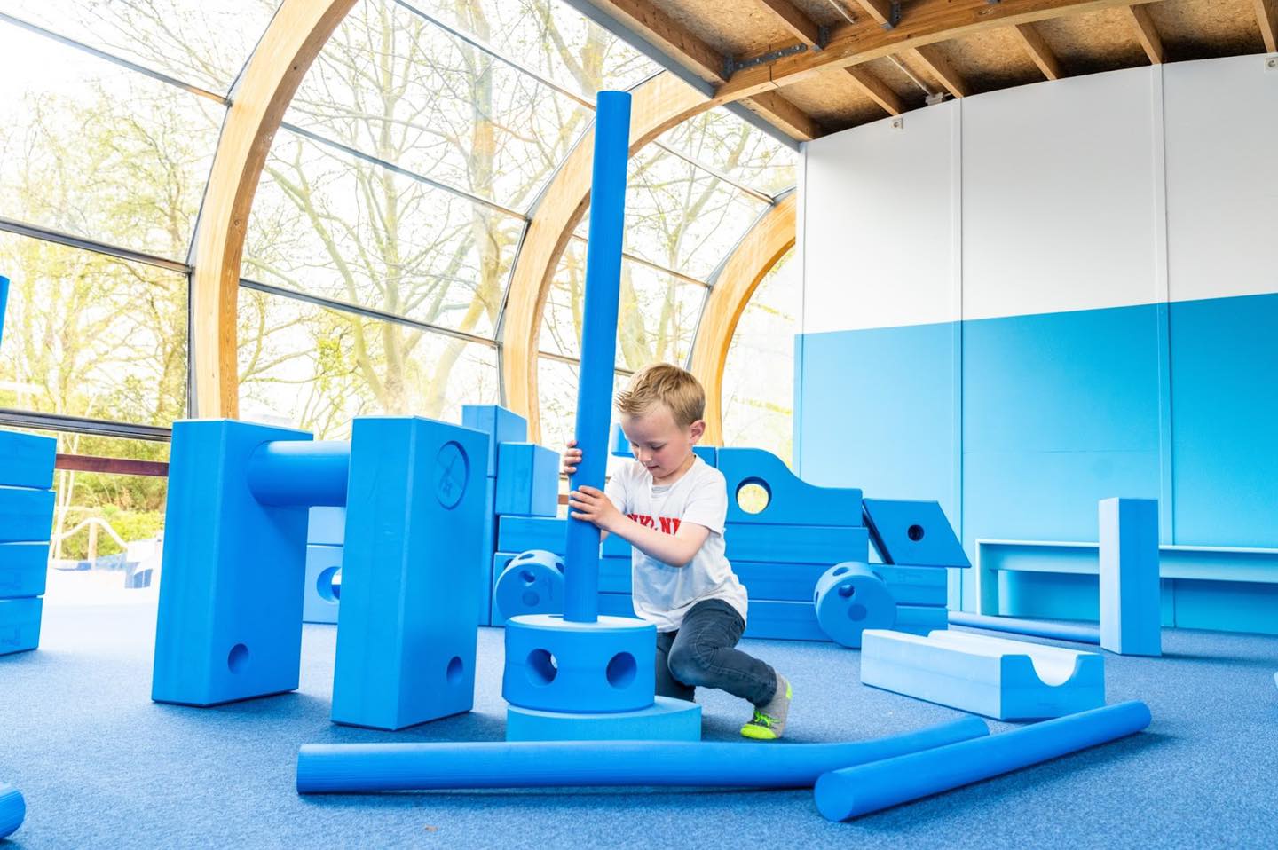 Children collaborating and building a custom structure using large blue foam Imagination Playground blocks in an outdoor setting.