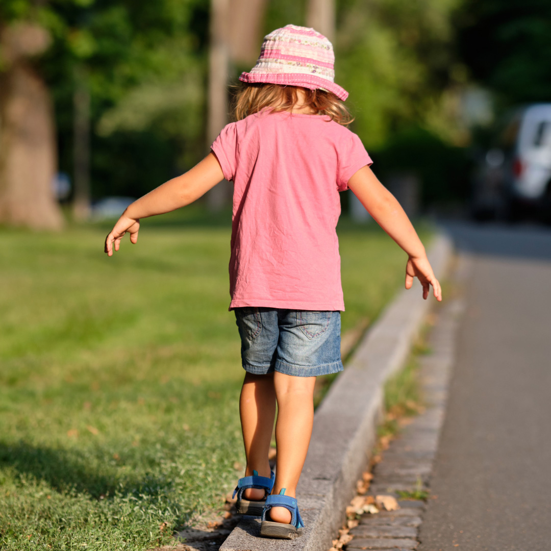A young girl balancing as she walks across a curb outdoors.