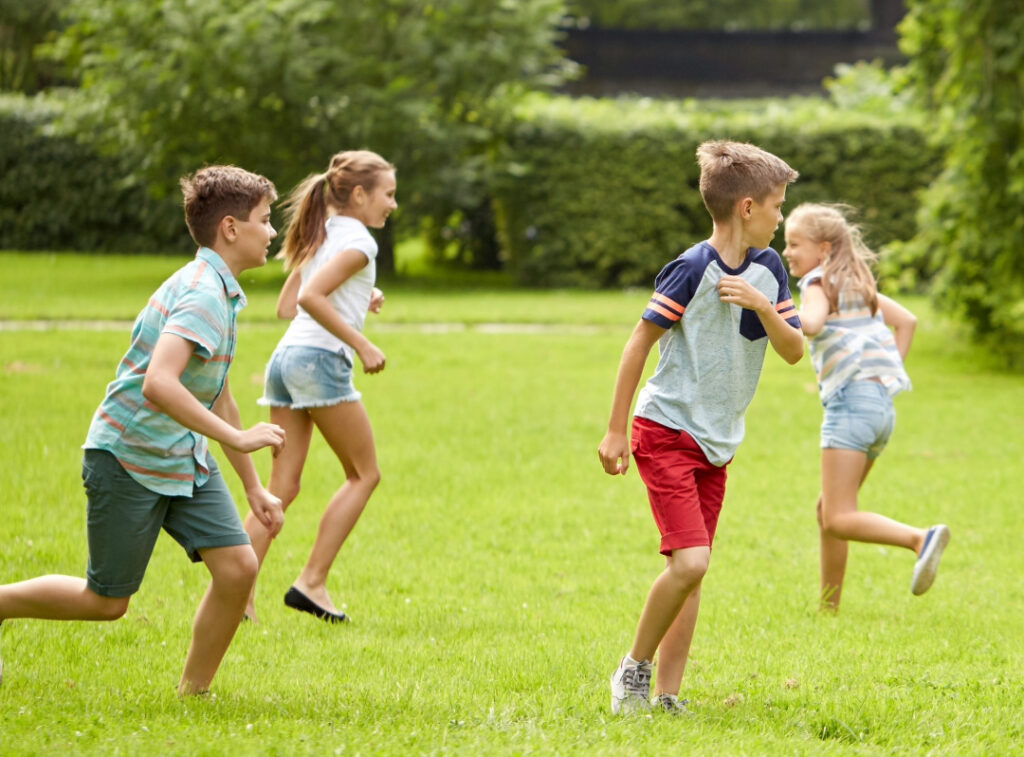 Children running, playing, and jumping together on a grassy field outdoors.