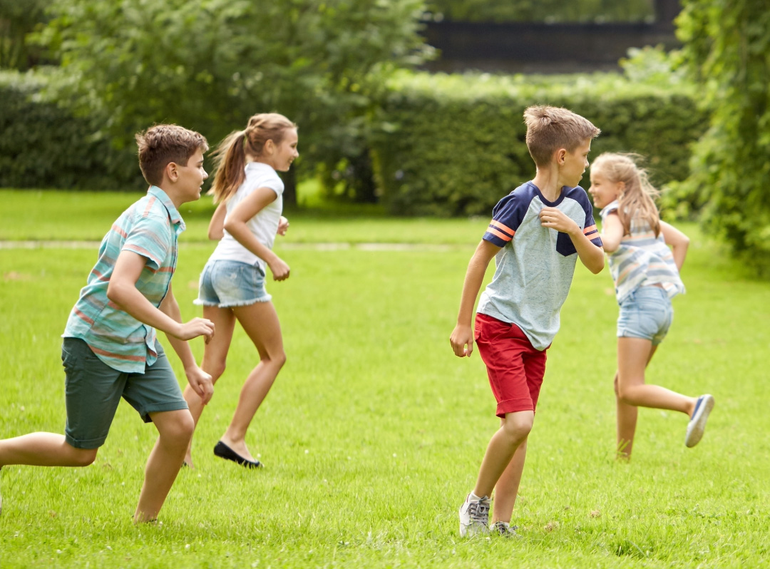 Children running, playing, and jumping together on a grassy field outdoors.