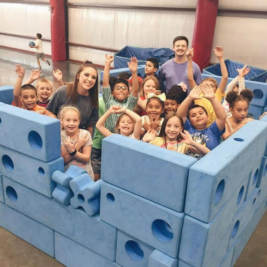 A group of children playing together inside a large structure built from giant blue foam blocks.